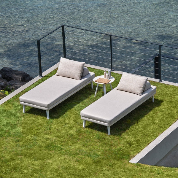 "Light gray pool loungers with textured cushions on green grass, paired with a small white side table."