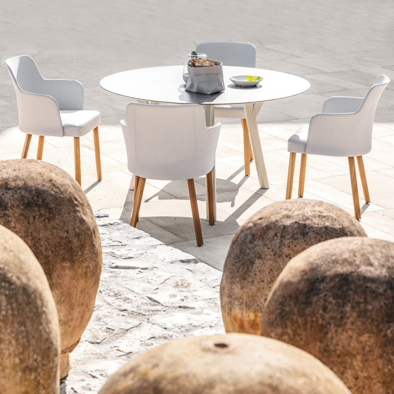 Modern white dining table and chairs with wooden legs, set against a neutral stone background and rustic clay pots.