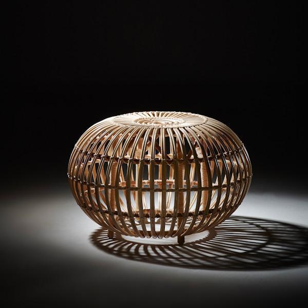 Natural woven rattan basket with a circular design, showcasing light and shadow play in a dark setting.