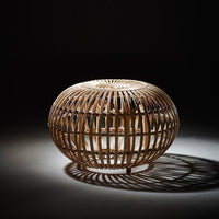 Natural woven rattan basket with a circular design, showcasing light and shadow play in a dark setting.