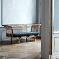 Light rattan sofa with a dark gray cushion against a pale blue wall and wooden floor, showcasing modern elegance.