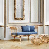 Rattan sofa with blue cushions, featuring a woven pattern and natural wood finish, set against an elegant interior backdrop.