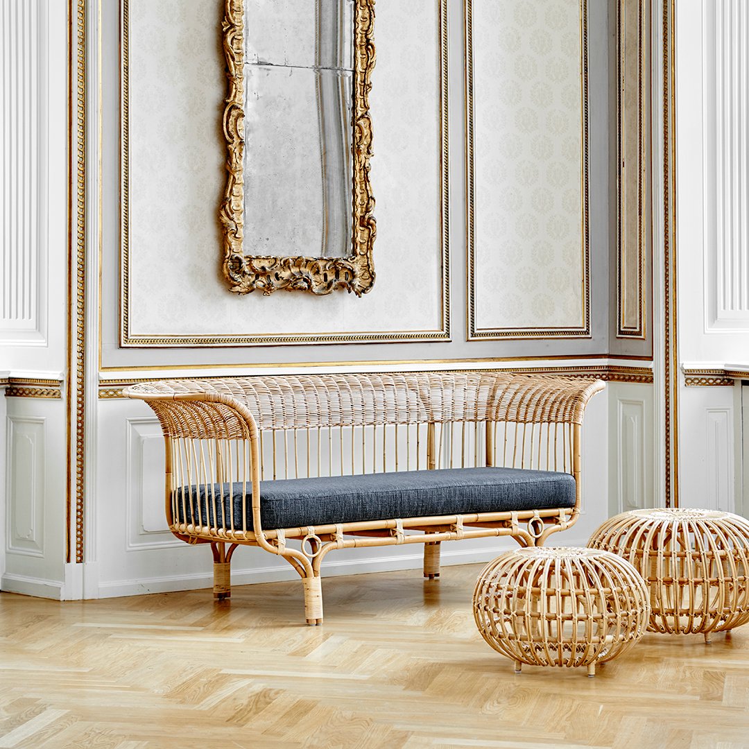 Natural rattan loveseat with a dark gray cushion, set in a luxurious, patterned interior.
