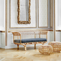 Natural rattan loveseat with a dark gray cushion, set in a luxurious, patterned interior.