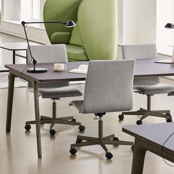 Gray upholstered office chairs around a dark wood table, featuring a vibrant green accent chair in a bright, modern workspace.