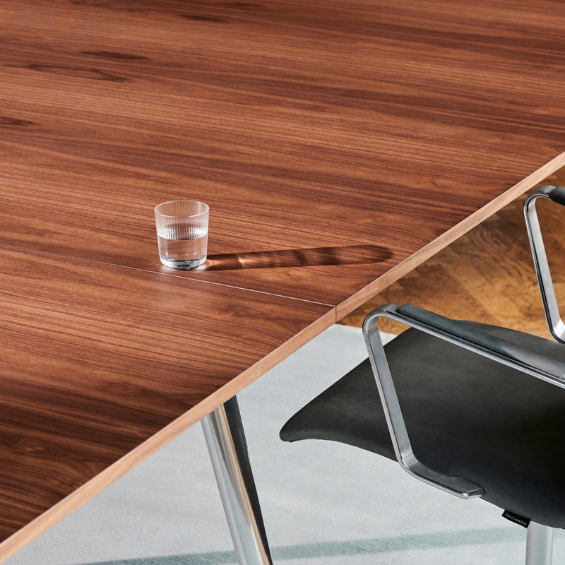 Rich walnut wood grain tabletop with subtle light reflections and contrasting sleek metallic chair.