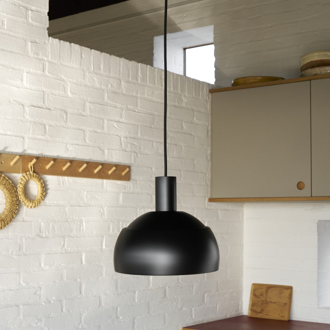Black pendant light hanging in a kitchen with white brick wall and wooden cabinets.