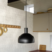 Black pendant light hanging in a kitchen with white brick wall and wooden cabinets.