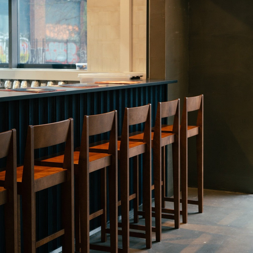 "Modern wooden bar stools with a rich brown finish against a sleek black and neutral backdrop."