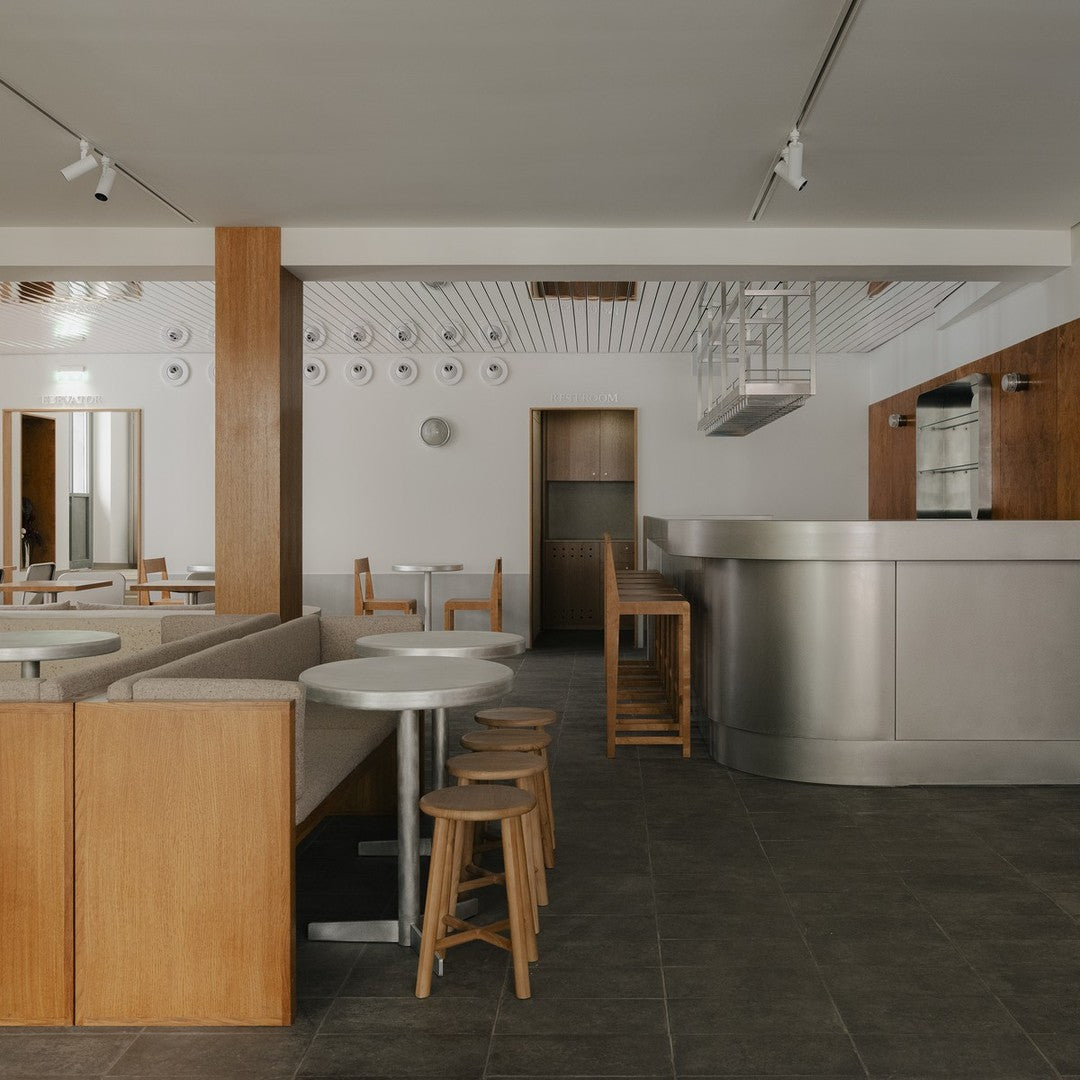 Modern café interior with warm wood tones, white surfaces, and sleek silver accents. Minimalist design with neutral colors.