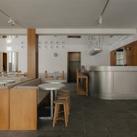 Modern café interior with warm wood tones, white surfaces, and sleek silver accents. Minimalist design with neutral colors.