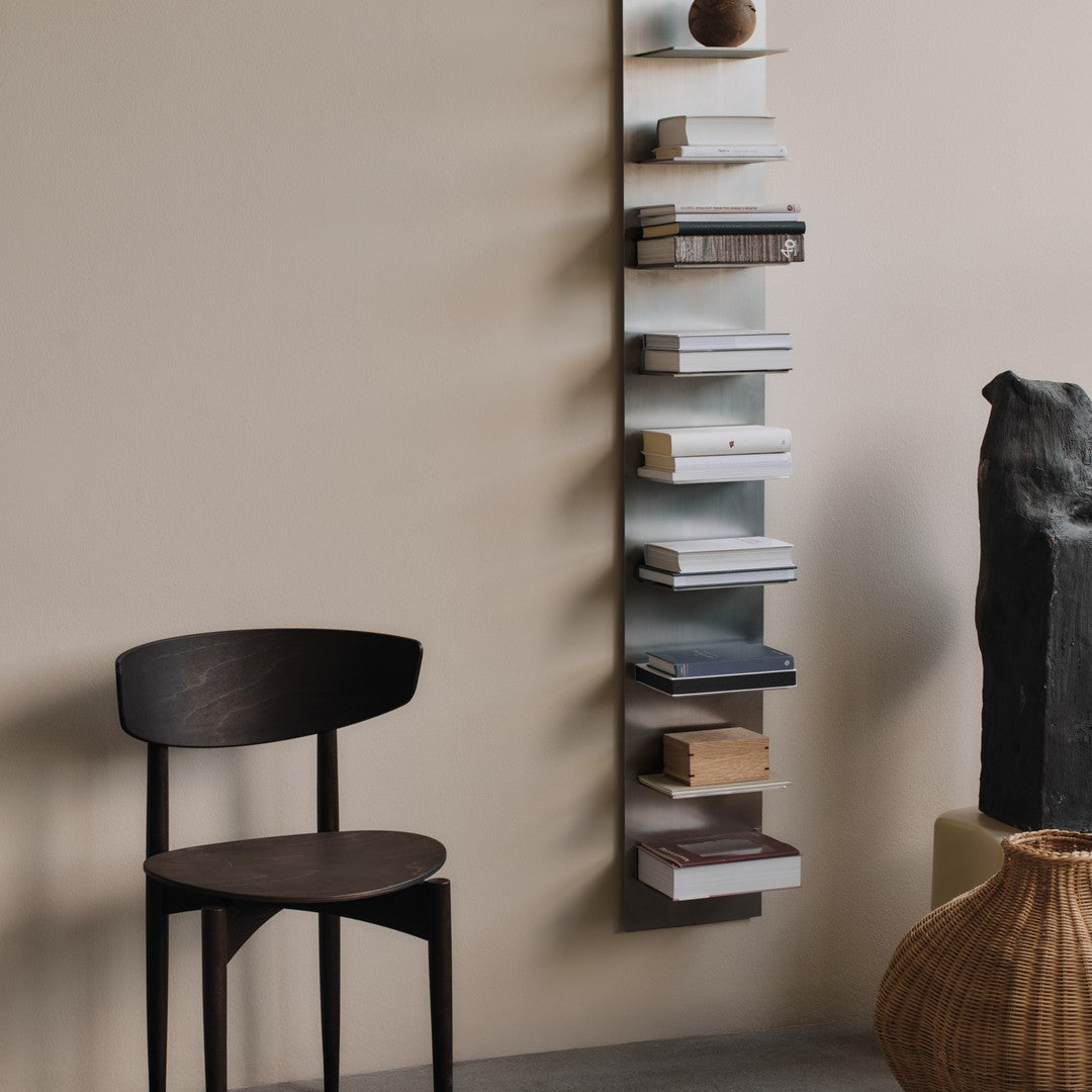 Minimalist metal bookshelf with gray, white, and black books against a soft beige wall, paired with a dark wooden chair.