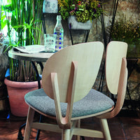 Light wood chair with a grey upholstered seat, surrounded by green foliage and rustic decor elements.