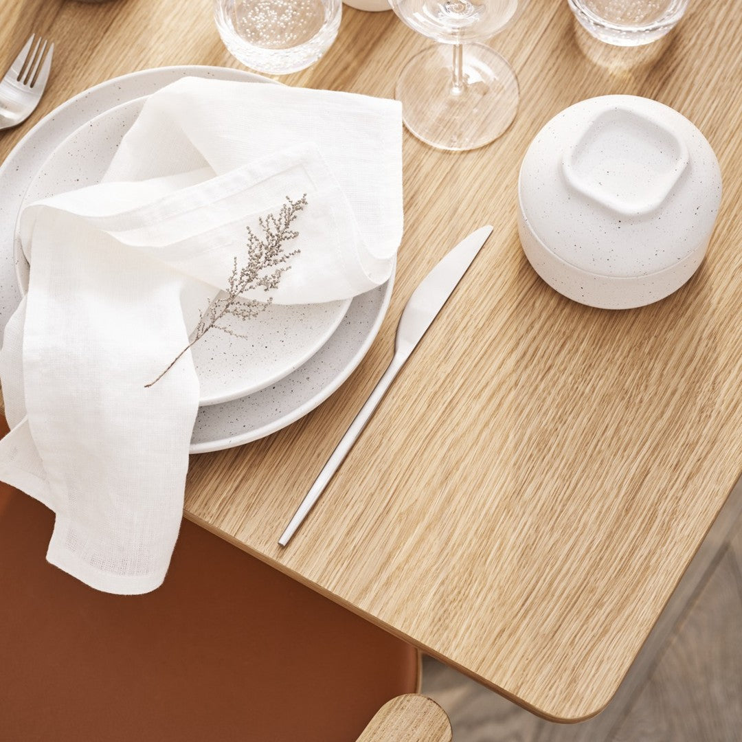 Elegant white dinnerware and linen napkin on natural wood table, featuring soft textures and minimalist design.