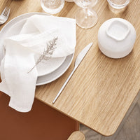 Elegant white dinnerware and linen napkin on natural wood table, featuring soft textures and minimalist design.
