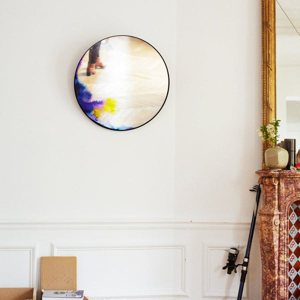 Colorful round wall mirror featuring soft blue, yellow, and white abstract patterns against a light backdrop.