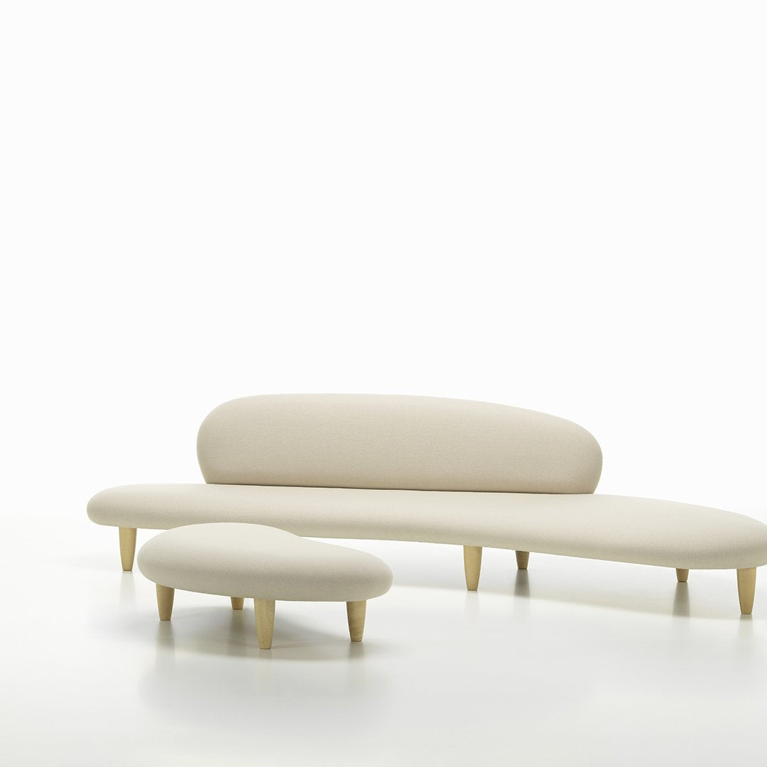 Beige modern sofa and ottoman with smooth curves and light wooden legs on a white background.