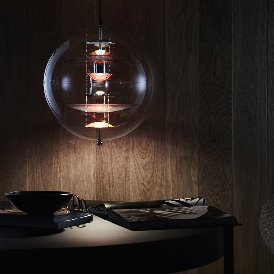 "Modern pendant light with clear glass, warm amber accents, and sleek metallic details against a dark wood backdrop."