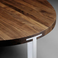 Round walnut wood tabletop with rich grain patterns and sleek silver metal accents. Elegant modern design.