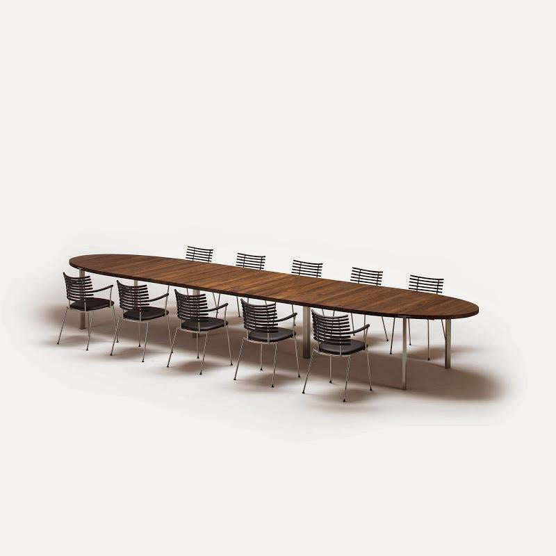 Long oval wooden dining table with a warm brown finish, paired with sleek silver and transparent chairs.