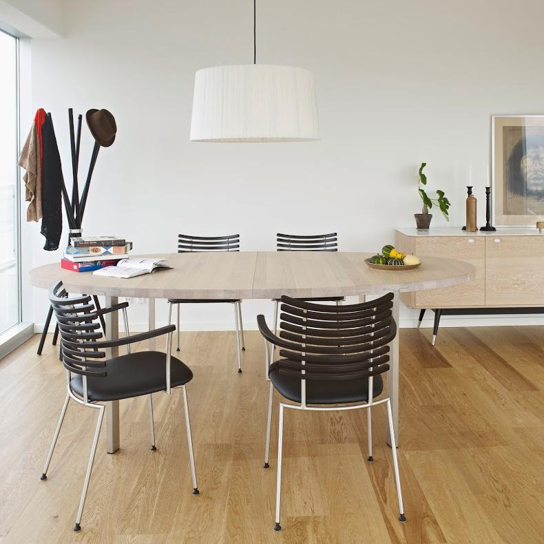 Modern round dining table with a light wood finish, complemented by sleek black striped chairs and warm oak flooring.