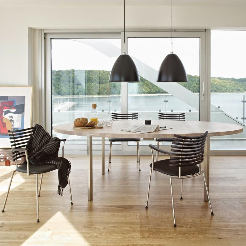 Modern round dining table with a light wood finish, surrounded by sleek black striped chairs under stylish black pendant lights.