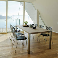 Modern wooden dining table with sleek metal legs, surrounded by black and chrome striped chairs on light wood flooring.