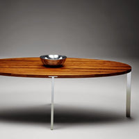 Sleek oval coffee table with rich brown wood grain and polished silver legs, minimalist design with modern elegance.