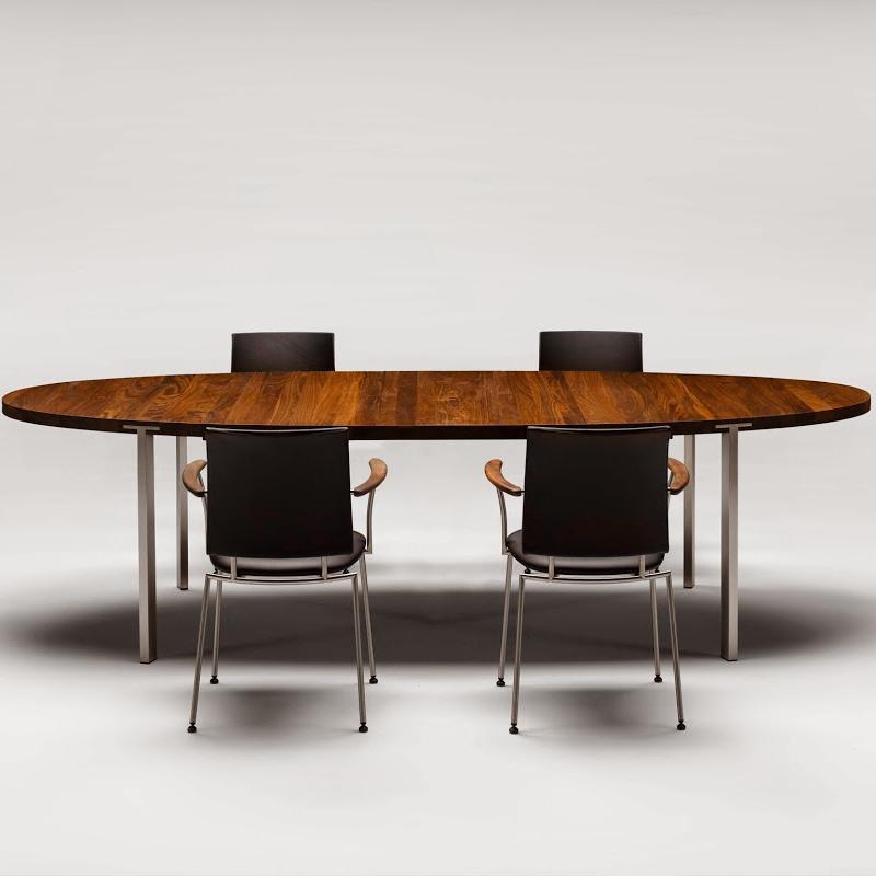 Oval wooden table with a rich brown finish and sleek metallic legs, surrounded by modern black chairs.