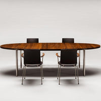Oval wooden table with a rich brown finish and sleek metallic legs, surrounded by modern black chairs.