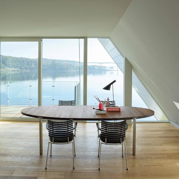 Modern round wooden table with sleek black and white striped chairs, against a serene lake view backdrop.
