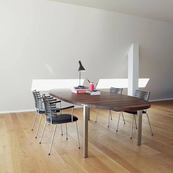 Modern wooden dining table with a walnut finish, complemented by sleek silver and black chairs in a minimalist setting.