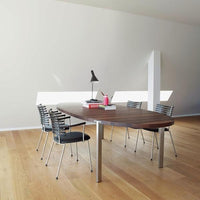 Modern wooden dining table with a walnut finish, complemented by sleek silver and black chairs in a minimalist setting.