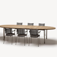 Wooden oval dining table with a natural finish and six black striped chairs featuring a modern design.