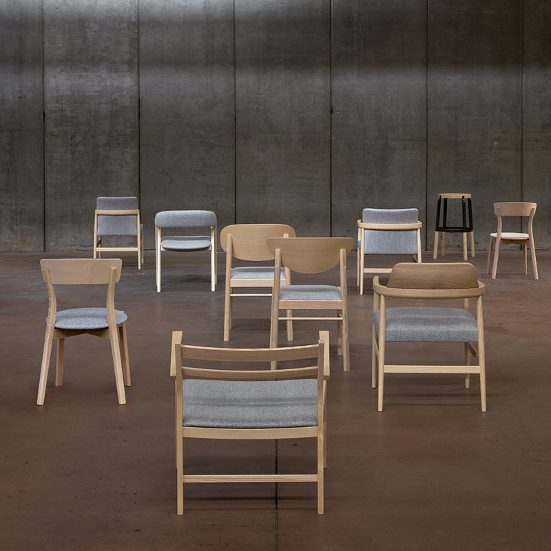 Assorted chairs in natural wood tones with gray and beige fabric patterns, set against a sleek industrial backdrop.