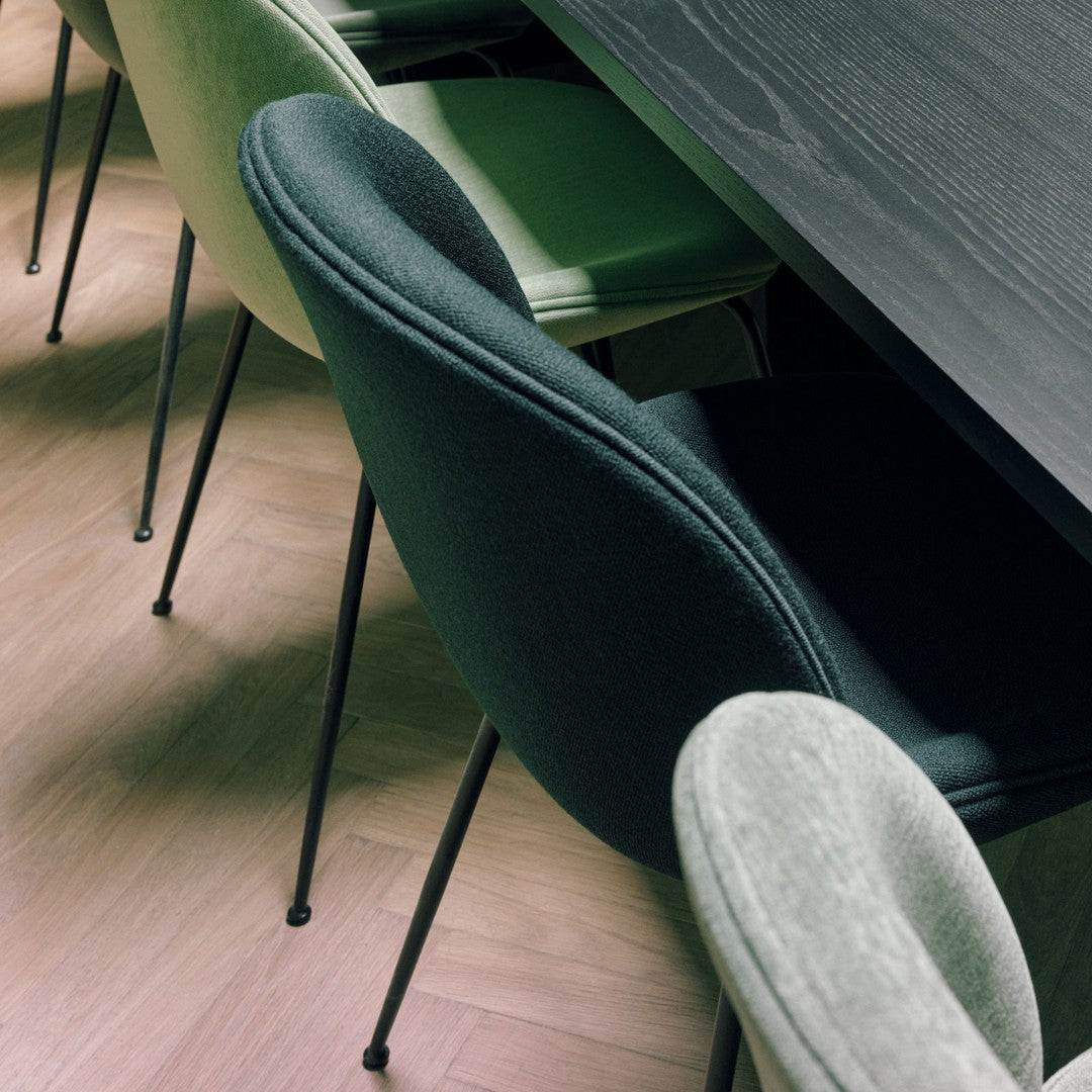 "Black, green, and grey chairs with soft upholstery, paired with a dark wooden table on light hardwood floor."