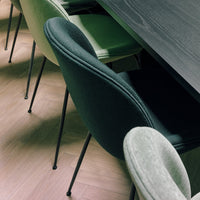 "Black, green, and grey chairs with soft upholstery, paired with a dark wooden table on light hardwood floor."