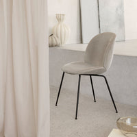 Soft grey velvet chair with a sleek black metal frame, set against light neutral backdrop. Modern and minimalist design.