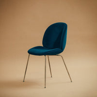 Teal velvet chair with a sleek design and chrome legs against a warm, neutral background.