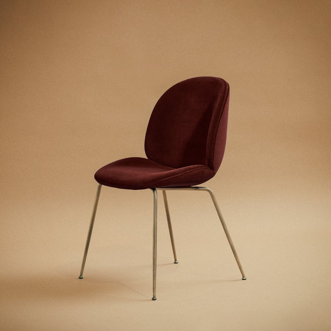 Elegant burgundy velvet chair with a smooth, rounded back and sleek metallic legs against a warm beige backdrop.