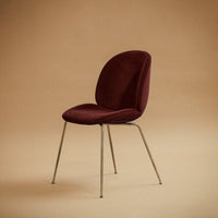 Elegant burgundy velvet chair with a smooth, rounded back and sleek metallic legs against a warm beige backdrop.