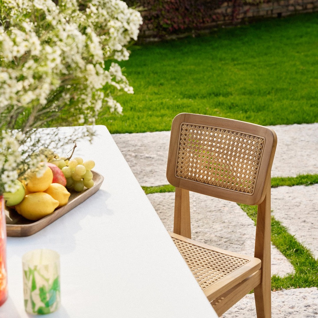 "Natural wood chair with woven cane back, paired with a bright white table and lush green outdoor grass."