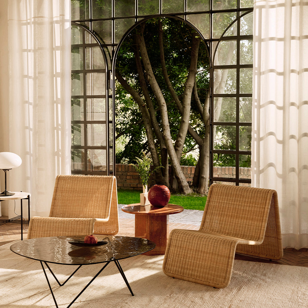 "Light natural rattan chairs and black marble table against a soft beige rug and airy white curtains."