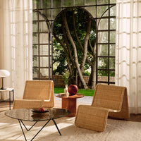 "Light natural rattan chairs and black marble table against a soft beige rug and airy white curtains."