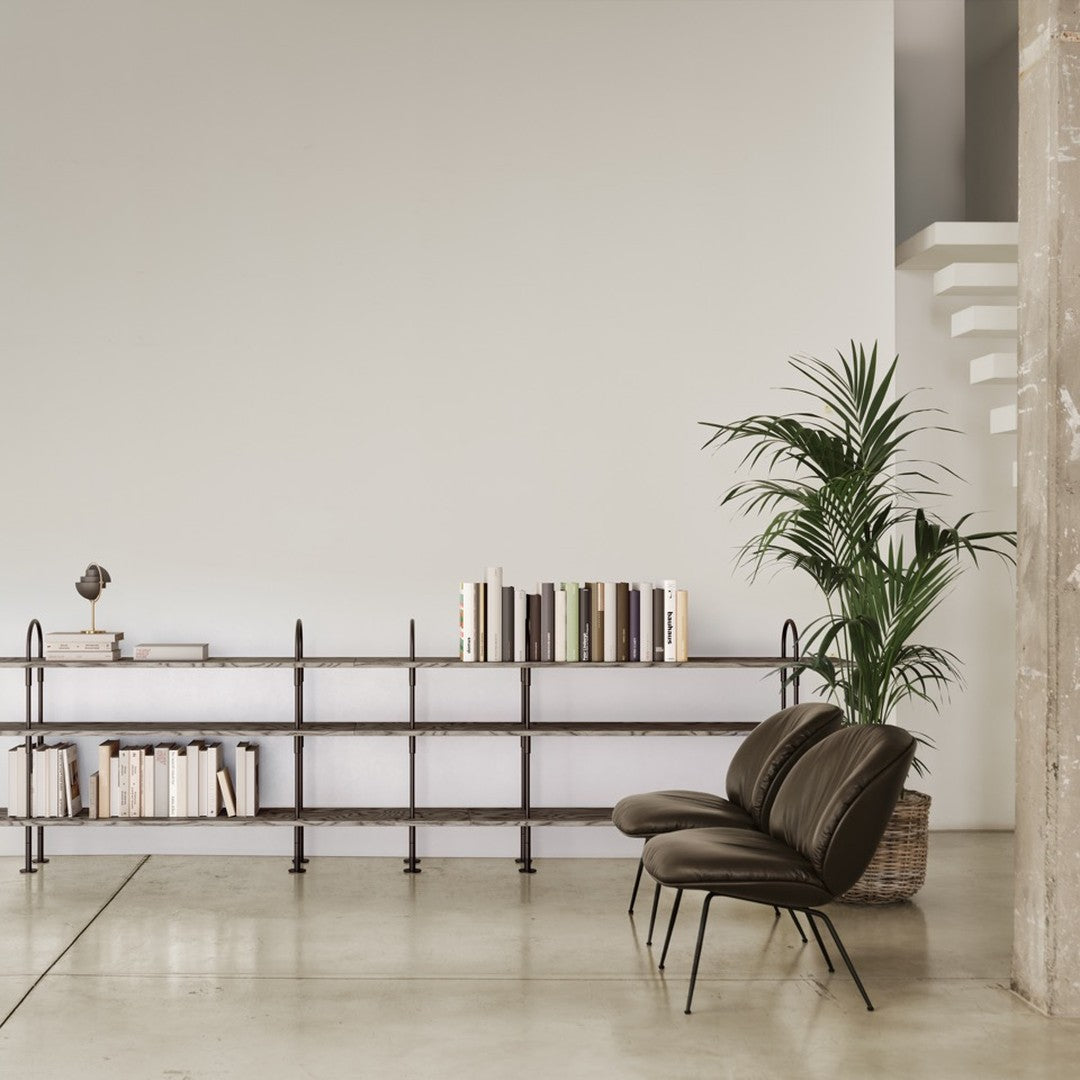 Modern bookshelf with light gray shelves, black metal accents, and neutral-toned books; sleek brown chairs in a minimalist setting.
