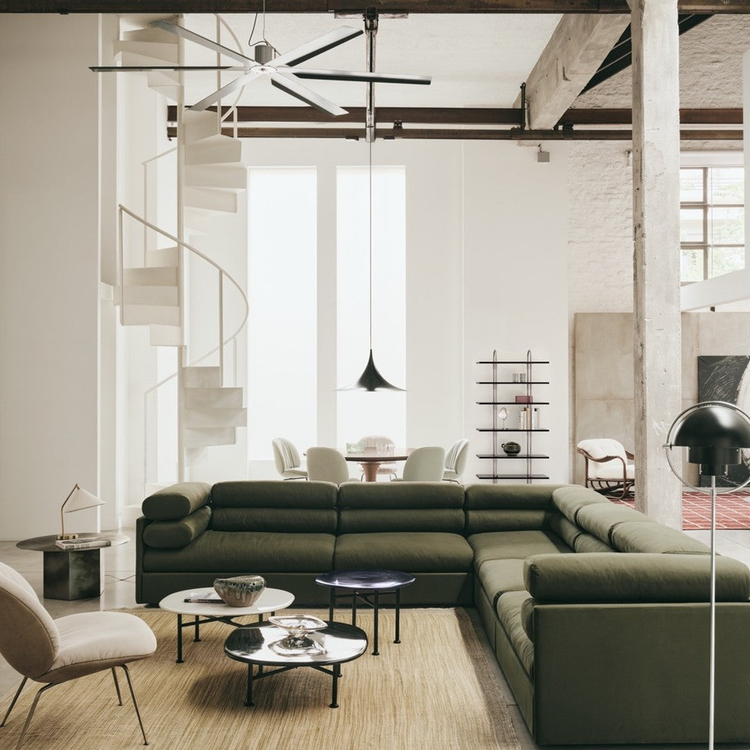 Modern green sectional sofa with sleek black and white accent tables in a minimalist, neutral-toned living space.