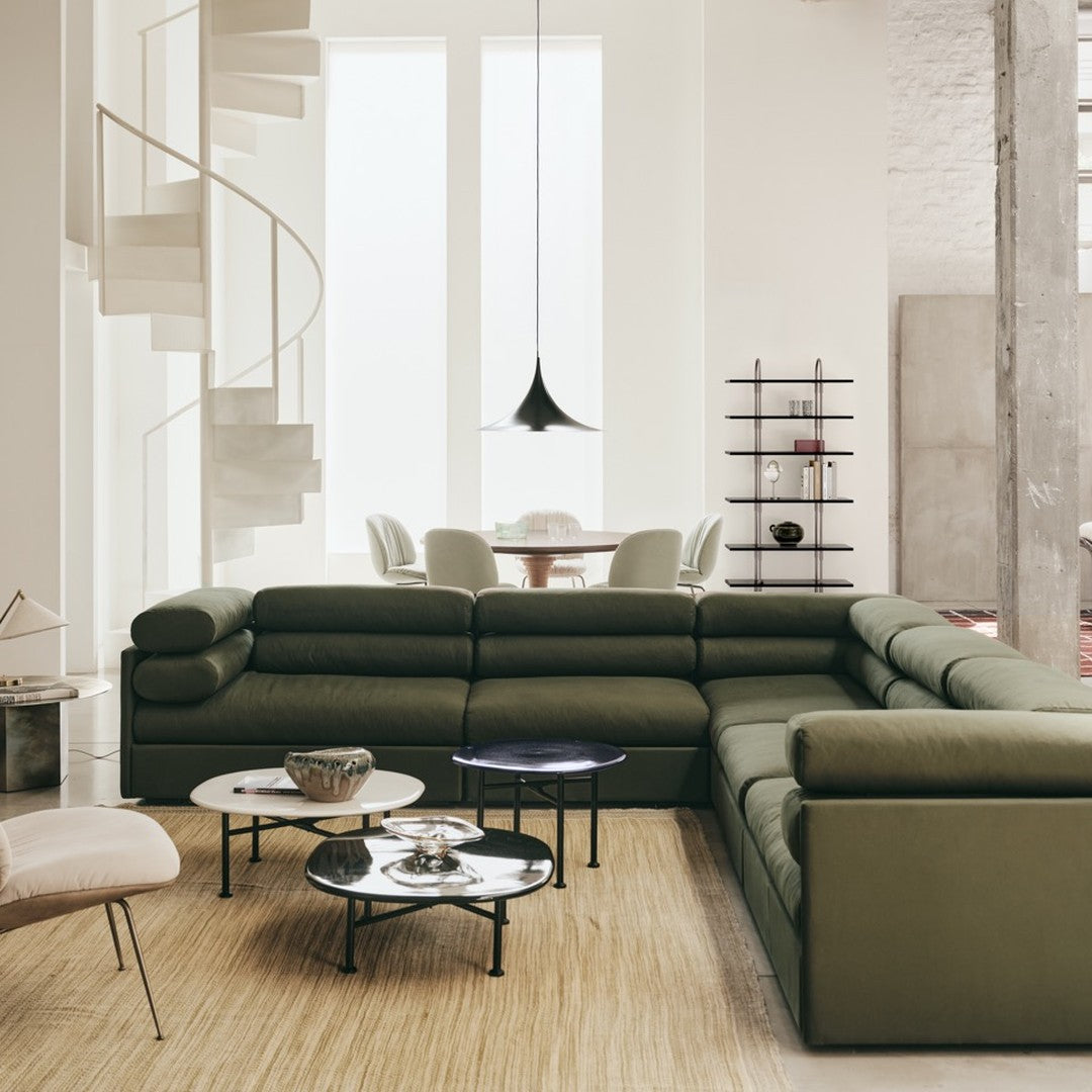 Olive green sectional sofa with black and white accent tables, neutral-toned decor in a bright, modern living space.