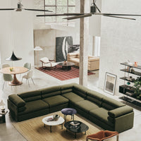 Olive green sectional sofa with round navy and white accent tables against a neutral backdrop and patterned red rug.