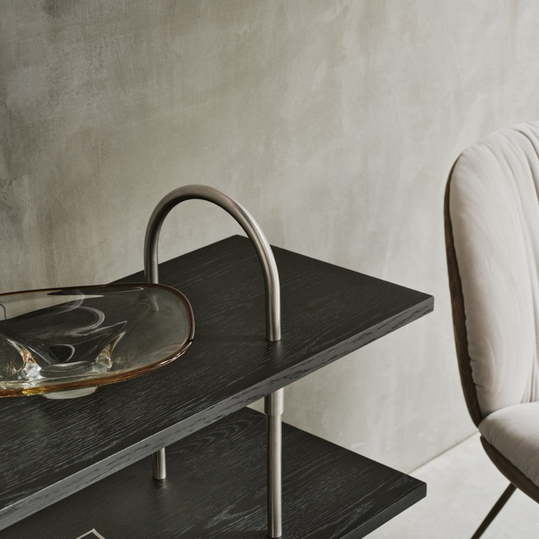 Black wooden shelf with sleek silver accents and a clear, amber glass dish, set against a neutral concrete backdrop.