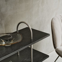 Black wooden shelf with sleek silver accents and a clear, amber glass dish, set against a neutral concrete backdrop.